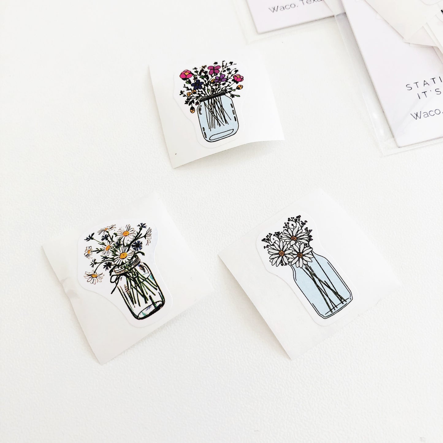 A photo showing three flower stickers from Shop Fleur Papier. The stickers feature different bouquets of flowers in mason jars, with one bouquet featuring colorful flowers and the other two featuring white daisies.