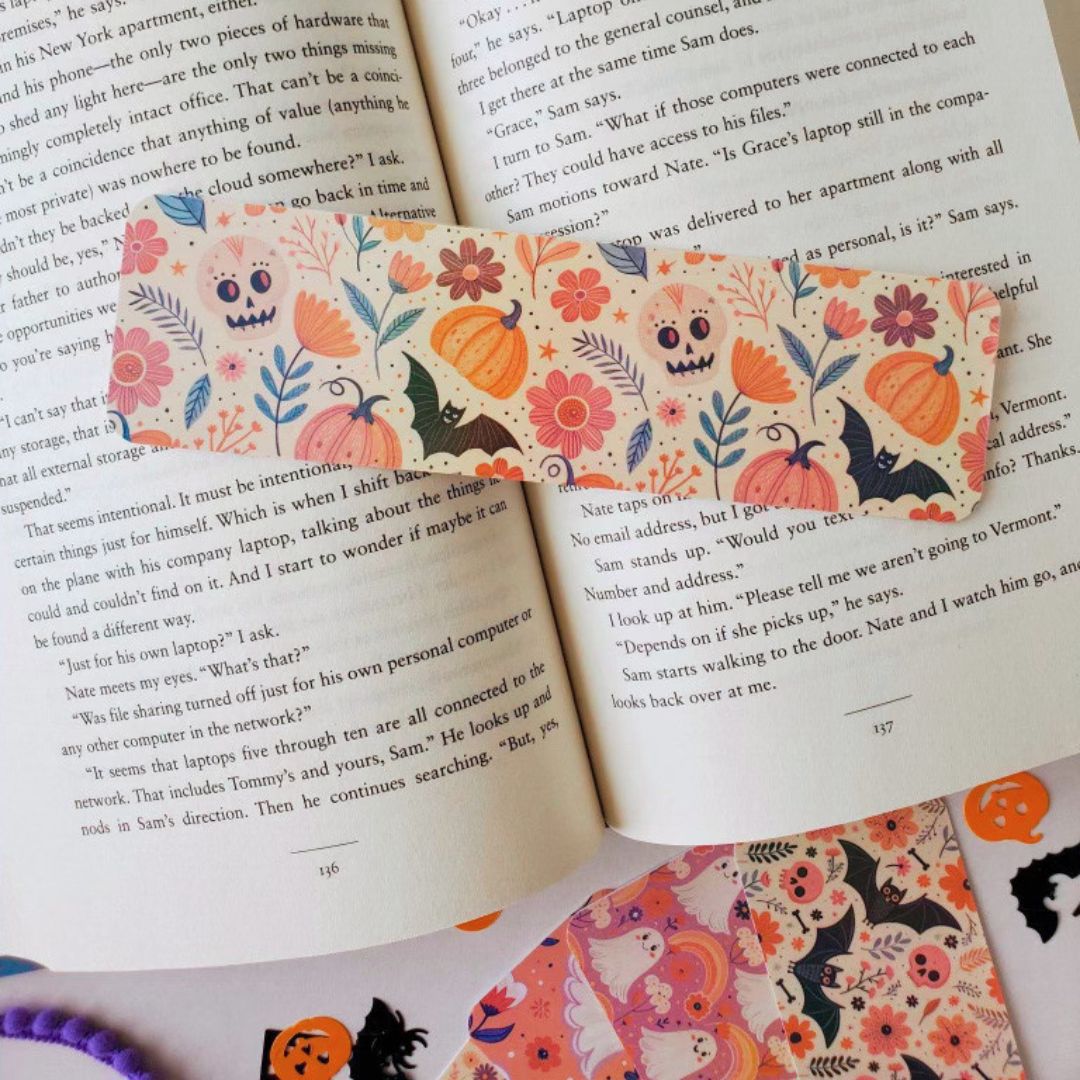 Flatlay of pastel spooky bookmarks featuring cute ghost patterns and floral fall elements, photographed on top of a novel.