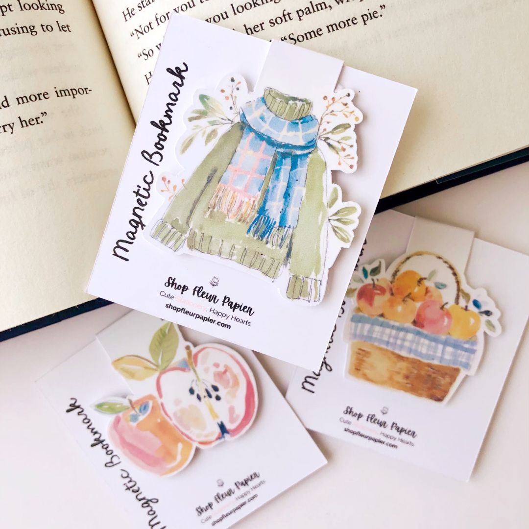 Collection of illustrated magnetic book marks featuring a basket of apples, a sweater, and other designs on a white background.