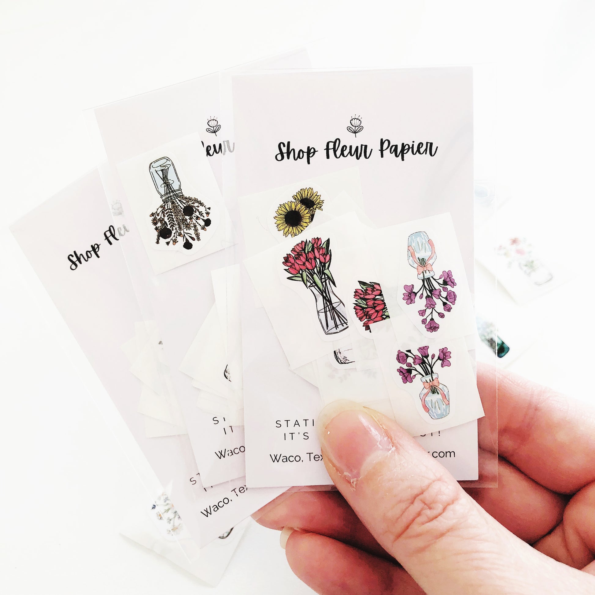 A hand holding a sheet of flower stickers in mason jars.