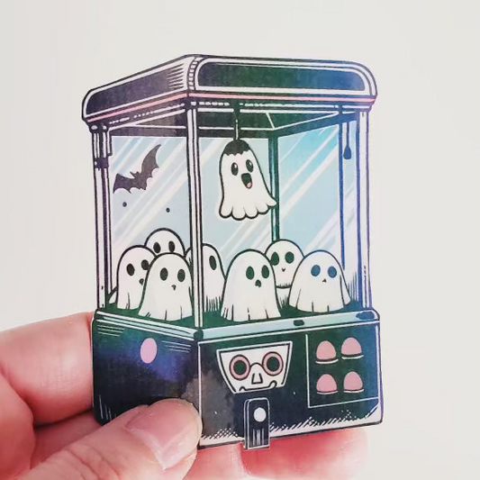 Close-up of spooky cute ghost claw machine sticker with holographic effect and pastel Halloween design.