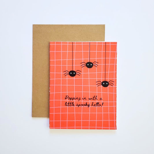 Orange grid-patterned card with spider design and text, featuring a brown envelope on a light gray background.