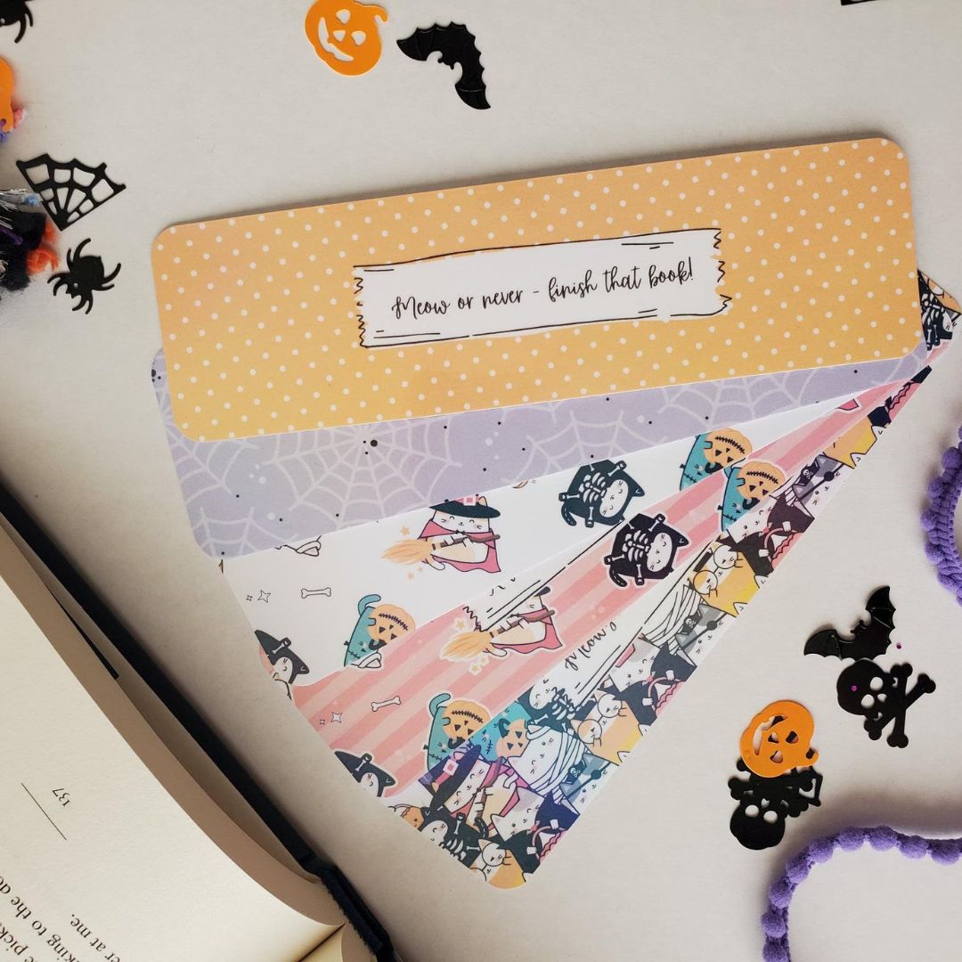 Colorful Halloween bookmark with cats in costume carrying pumpkins and candy on pink and orange stripes.